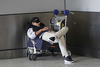 A traveler takes a nap as he waits for a ride outside Miami International Airport on July 1, 2022, in Miami. A Gallup survey released Monday, April 15, 2024, reports a majority of Americans say they would feel better if they could have more sleep. But in the U.S., where the ethos of grinding and pulling yourself up by your own bootstraps is ubiquitous, getting enough sleep can seem like a dream. (AP Photo/Wilfredo Lee, File)